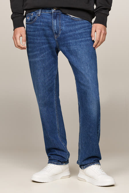 Jean droit bleu marine de TOMMY JEANS, avec une légère usure et des baskets blanches.