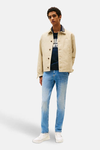 Jean slim fit bleu de TOMMY JEANS, associé à une veste beige et des baskets blanches.