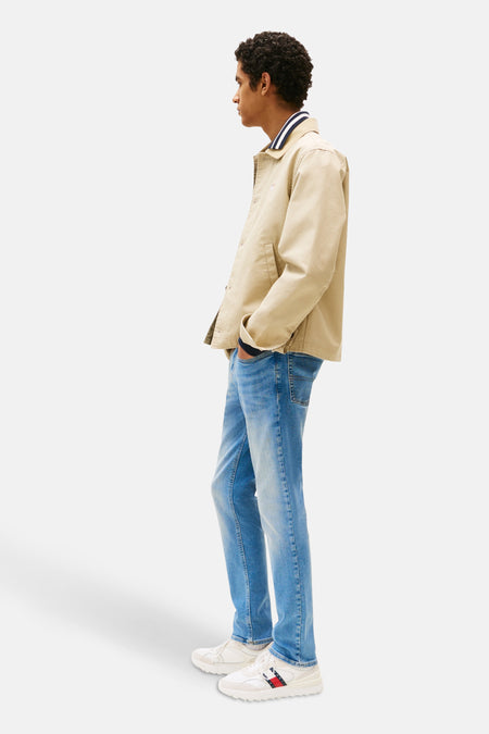 Jean slim fit en denim par TOMMY JEANS, légèrement lavé, associé à une veste beige.
