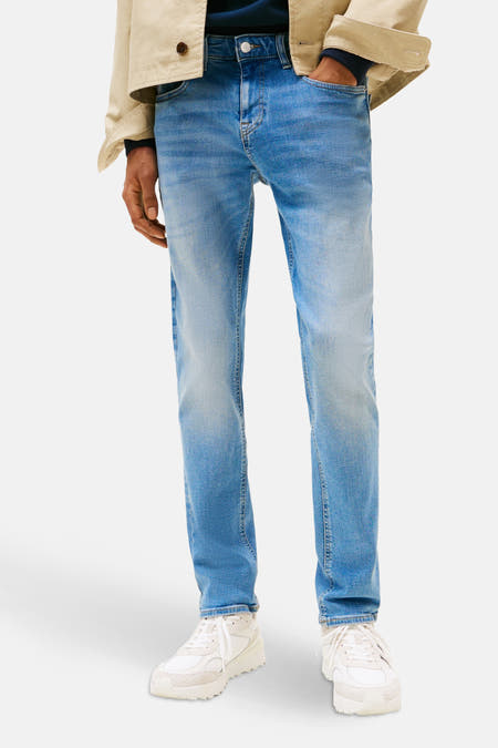 Jean slim fit en denim bleu moyen de Tommy Jeans, avec une polo blanche et un chapeau rouge.