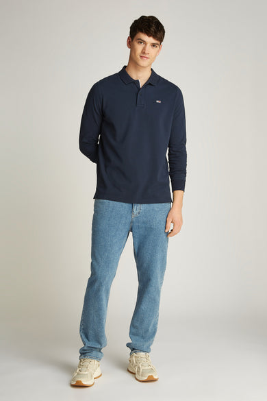Polo bleu avec des manches longues de TOMMY JEANS, porté avec des jeans et des baskets blanches.