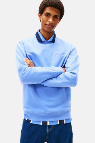 Pull-over bleu de TOMMY JEANS avec col rond et logo sur la poitrine, associé à des jeans larges.