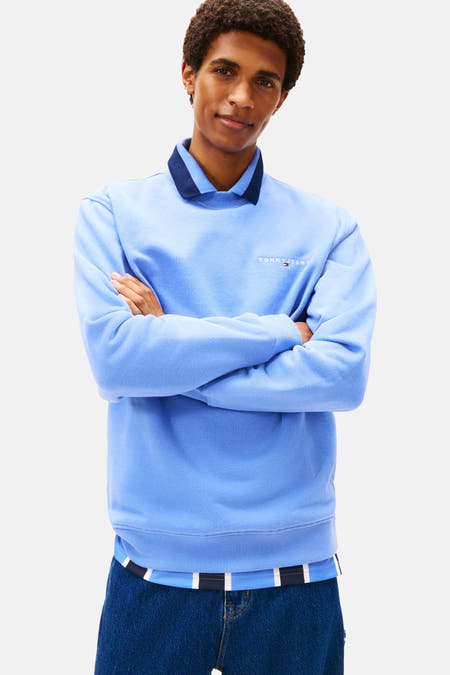 Pull-over bleu de TOMMY JEANS avec col rond et logo sur la poitrine, associé à des jeans larges.