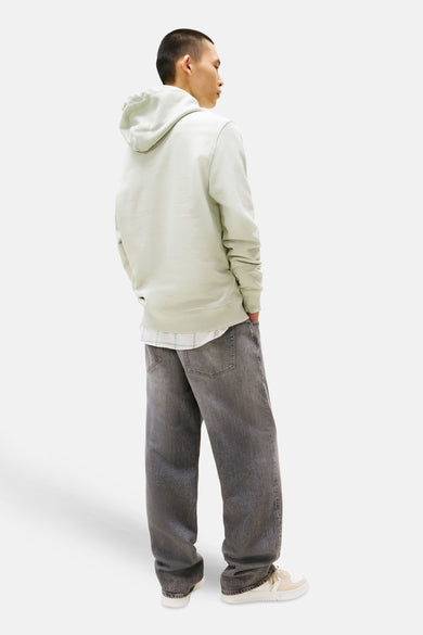 Sweater vert de TOMMY JEANS avec un capuchon, associé à des jeans gris larges et des baskets blanches.