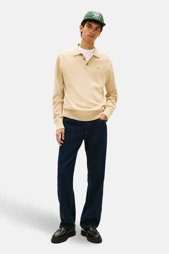 Beige trui van TOMMY JEANS, met lange mouwen, polokraag, een witte T-shirt eronder en blauwe jeans.

