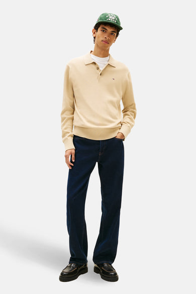Beige trui van TOMMY JEANS, met lange mouwen, polokraag, een witte T-shirt eronder en blauwe jeans.
