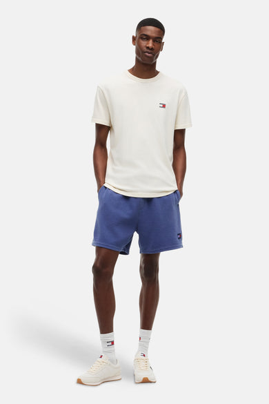 T-shirt à manches courtes de couleur crème de TOMMY JEANS, avec petit logo sur la poitrine, porté par un homme avec un short bleu.