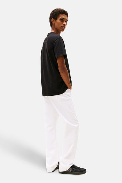 T-shirt noir à manches courtes de TOMMY JEANS, avec un col rond et porté avec un pantalon blanc.