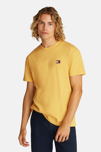 T-shirt jaune à manches courtes de TOMMY JEANS, vu de dos, avec des shorts bleus marine, des chaussettes blanches et des baskets.