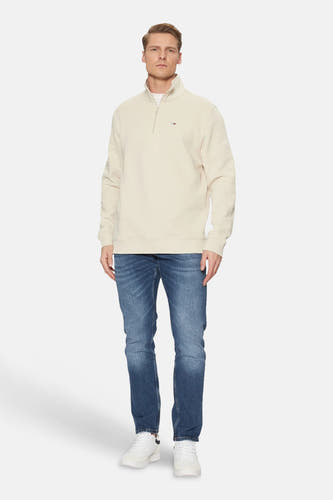 Beige ronde hals sweater van TOMMY JEANS, met halve rits en klein logo, gedragen met blauwe jeans en witte sneakers, front view.