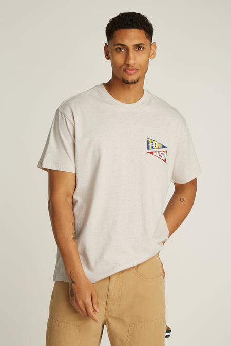 T-shirt écru à manches courtes de TOMMY JEANS, avec un petit logo drapeau sur la poitrine et le modèle porte un pantalon kaki.