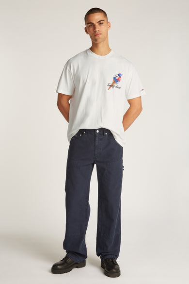 T-shirt blanc à manches courtes de TOMMY JEANS, avec une impression d'un glaçon, associé à un pantalon bleu marine et des chaussures noires.