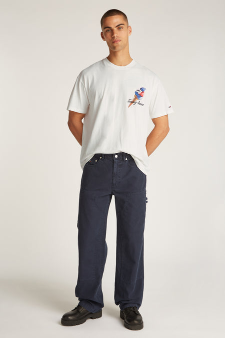 T-shirt blanc à manches courtes de TOMMY JEANS, avec une impression d'un glaçon, associé à un pantalon bleu marine et des chaussures noires.