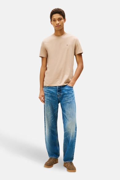 T-shirt beige à manches courtes de TOMMY JEANS, porté avec des jeans bleus et des chaussures marrons.