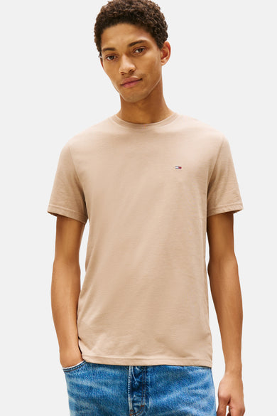 T-shirt beige à manches courtes de Tommy Jeans, avec un petit logo sur la poitrine, porté avec un jean bleu.