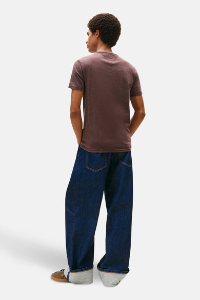 T-shirt marron à manches courtes de TOMMY JEANS, avec des jeans bleus foncés décontractés et des chaussures marrons.