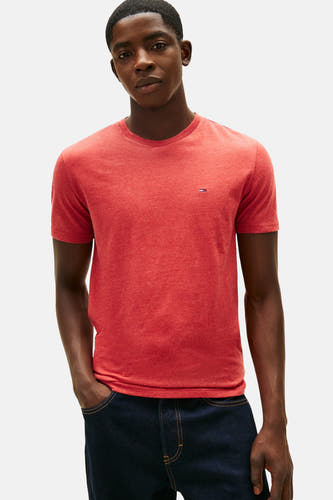 T-shirt rouge à manches courtes de TOMMY JEANS, porté avec des jeans bleus foncés larges et des baskets, accompagné d'une sacoche noire.