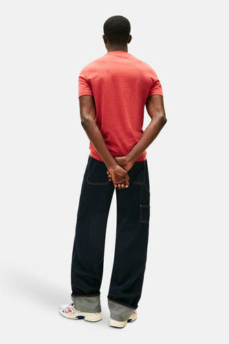 T-shirt rouge à manches courtes de Tommy Jeans, dos, porté avec des jeans foncés et des sneakers blanches.