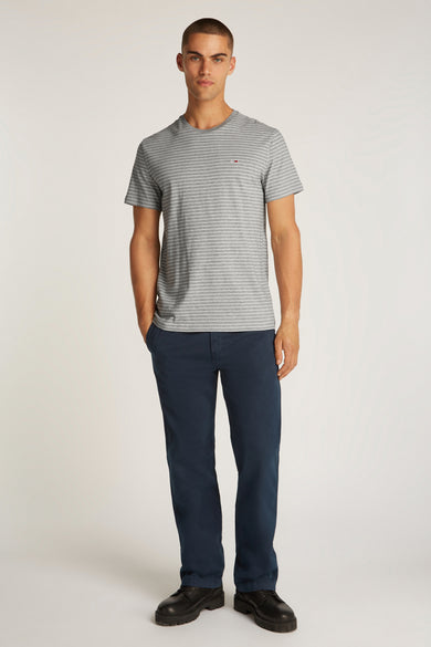 T-shirt gris rayé à manches courtes de TOMMY JEANS, porté avec un pantalon bleu marine et des chaussures noires.