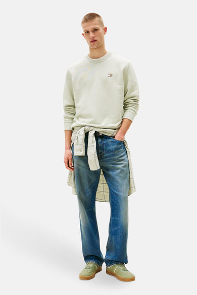 Pull-over vert de TOMMY JEANS, avec un petit logo brodé sur la poitrine, associé à une chemise à carreaux et des jeans bleus.