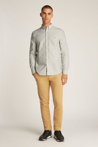 Chemise rayée gris clair et gris foncé Tommy Tommy Jeans avec des manches longues, associée à un pantalon beige et des baskets noires.