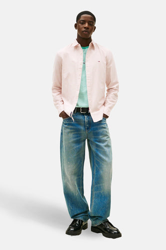 Een man met een gestreept overhemd, jeans en zwarte schoenen.