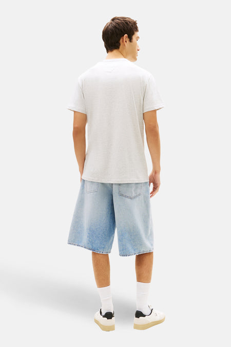 T-shirt gris à manches courtes TOMMY JEANS, vu de dos, associé à un short en jean ample, des chaussettes blanches et des baskets crème.