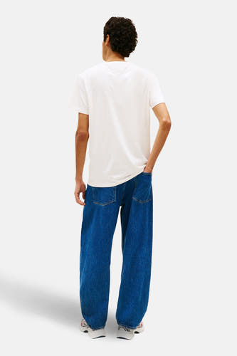 T-shirt blanc à manches courtes Tommy Jeans, vu de dos, porté avec un jean bleu ample et des baskets blanches.