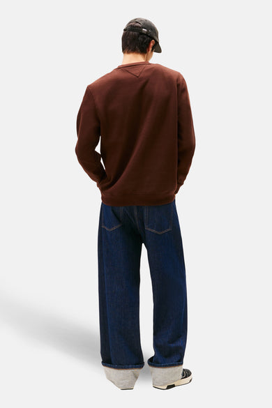 Pull marron de TOMMY JEANS, vu de l'arrière, associé à un jean bleu foncé et une casquette.