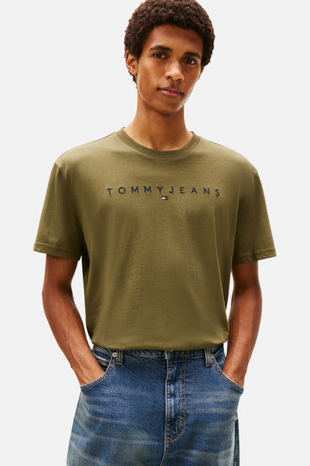 T-shirt vert avec manches courtes de TOMMY JEANS, avec un sac à dos en denim bleu sur l'épaule et des jeans larges.