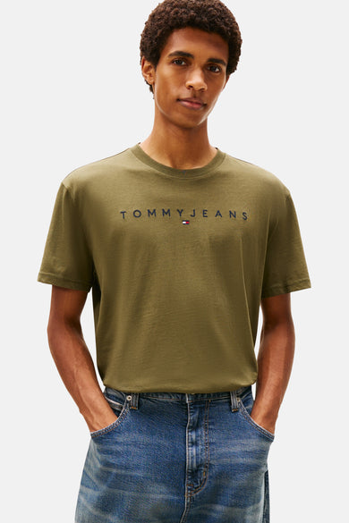 T-shirt vert avec manches courtes de TOMMY JEANS, avec un sac à dos en denim bleu sur l'épaule et des jeans larges.
