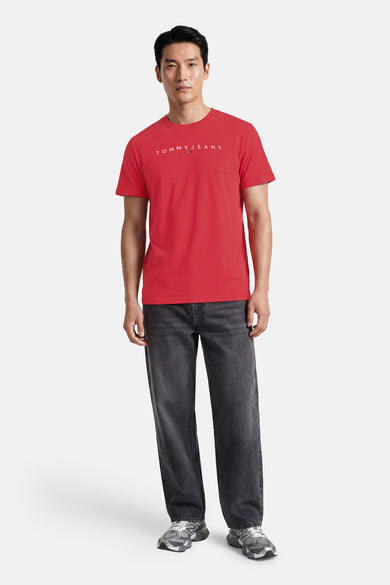 Rode korte mouw T-shirt van TOMMY JEANS met wit logo op borst, gedragen door model in lifestyle pose