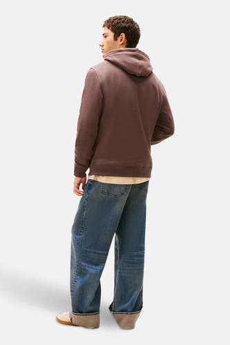 Bruine sweater met kap van TOMMY JEANS, met lange mouwen, en losse jeans.
