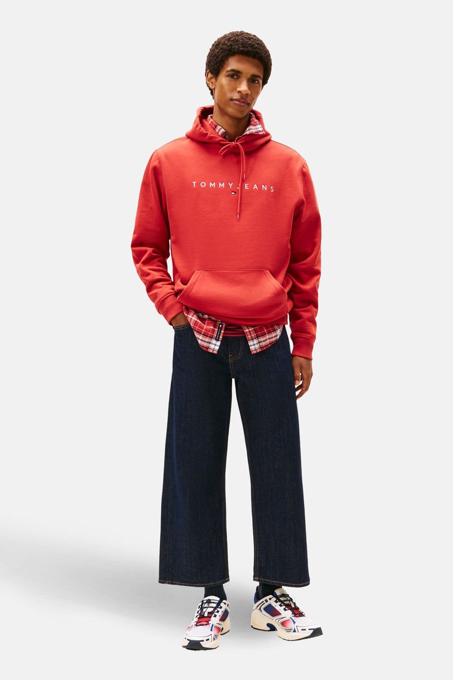 Rode sweater met kap van TOMMY JEANS, gedragen over een geruit overhemd en gecombineerd met wijde, donkerblauwe jeans.