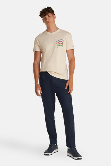 T-shirt beige à manches courtes de TOMMY JEANS, avec un logo coloré et associé à des pantalons bleu marine et des chaussures.
