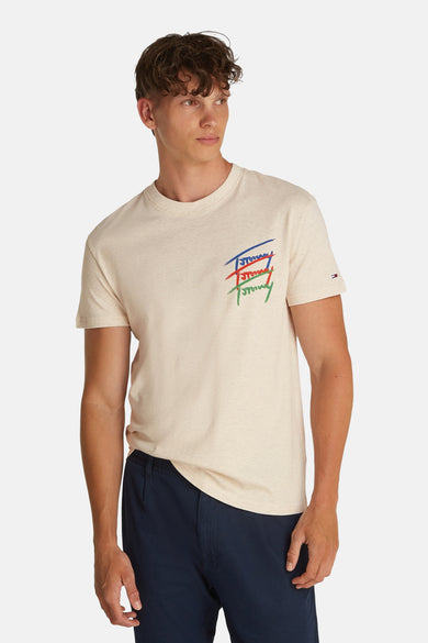 T-shirt beige à manches courtes de TOMMY JEANS, avec un logo coloré sur la poitrine et porté avec un pantalon bleu marine.