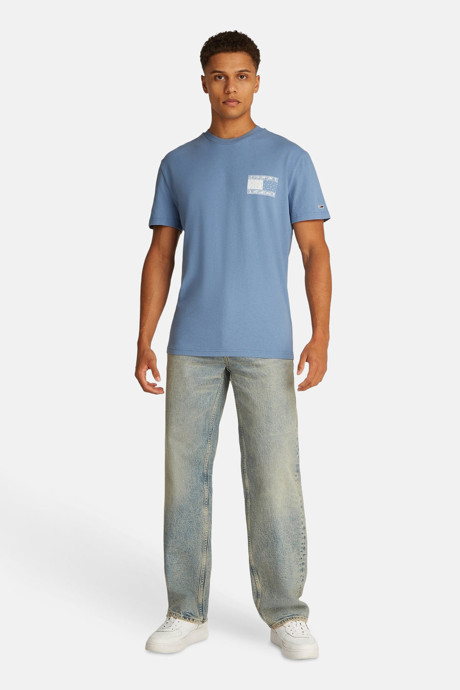 Man, blauw T-shirt, jeans, witte sneakers, staand, productfoto.
