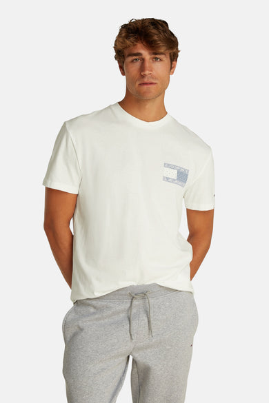 T-shirt blanc à manches courtes de Tommy Jeans, avec un petit logo bleu sur la poitrine et porté avec un pantalon de jogging gris.