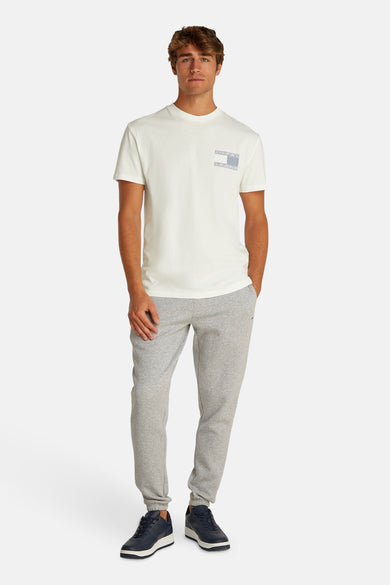 T-shirt blanc à manches courtes de TOMMY JEANS, avec un détail de logo subtil sur la poitrine, associé à des pantalons de jogging gris et des baskets bleu marine.