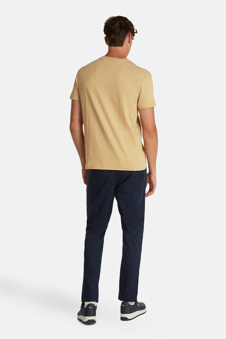 T-shirt beige à manches courtes de TOMMY JEANS, couleur unie et vue arrière, associé à des pantalons bleu marine et des baskets.