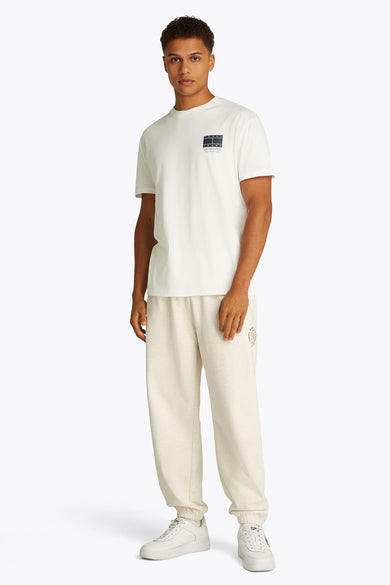 T-shirt blanc à manches courtes de TOMMY JEANS, avec un petit logo sur la poitrine, porté avec un pantalon de jogging et des baskets blanches.