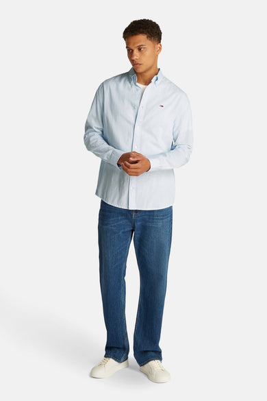 Chemise bleue claire à manches longues de Tommy Jeans, associée à des jeans bleus foncés et à des baskets blanches.