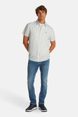 Chemise rayée bleue de TOMMY JEANS à manches courtes, portée avec des jeans et des baskets bleues.