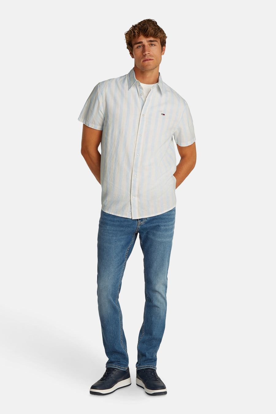 Chemise rayée bleue de TOMMY JEANS à manches courtes, portée avec des jeans et des baskets bleues.