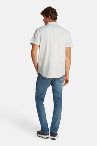 Chemise rayée bleue et blanche à manches courtes de TOMMY JEANS, portée avec des jeans bleus et des baskets bleu marine, vue de derrière.