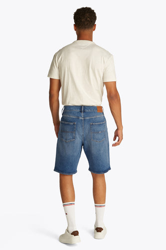 Man van achteren, T-shirt, jeansshorts, witte sokken en sneakers.
