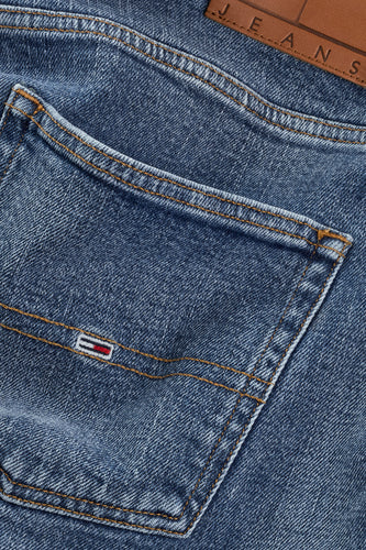 Close-up van blauwe jeans met zak en logo.

