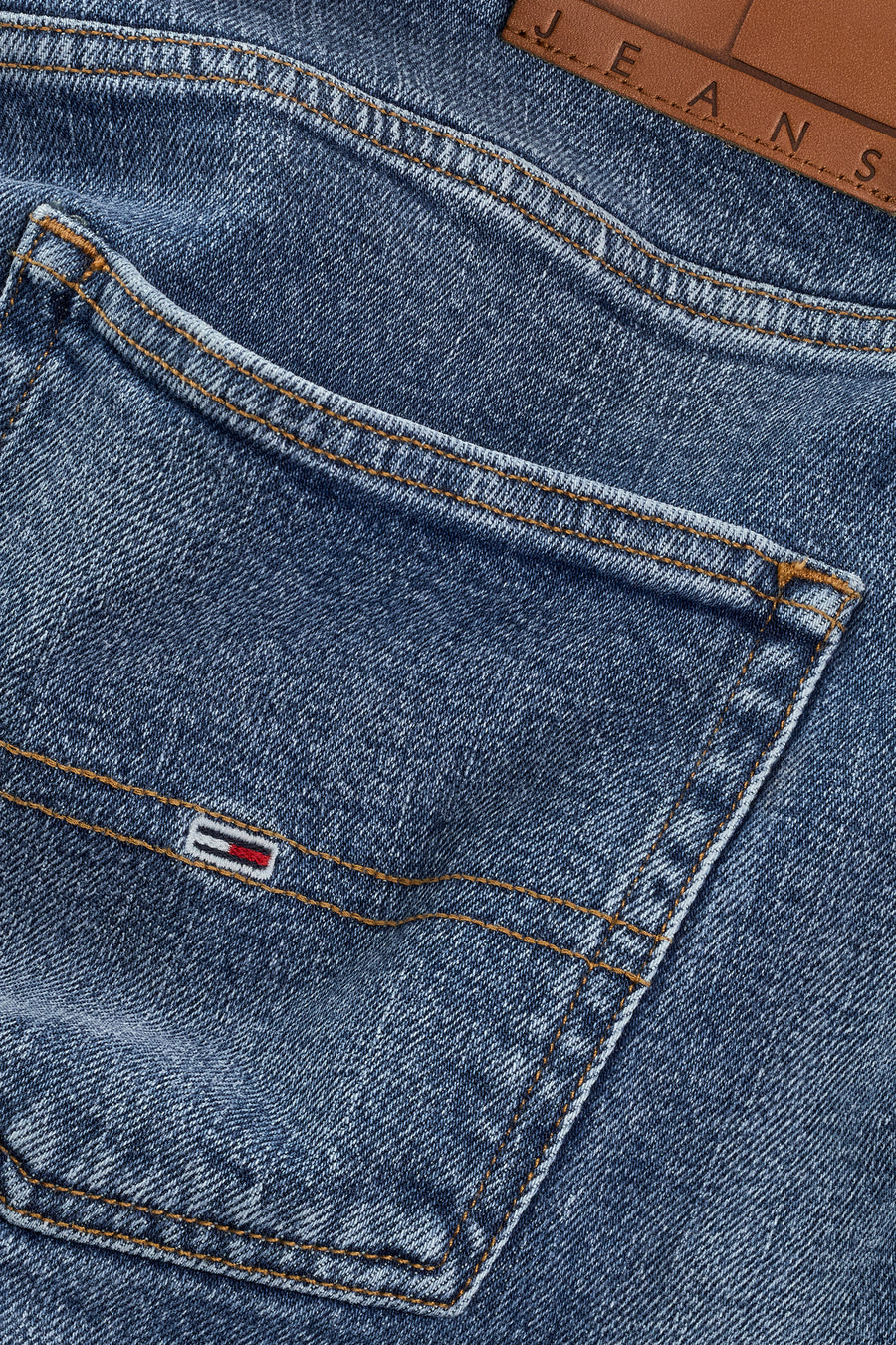 Close-up van blauwe jeans met zak en logo.
