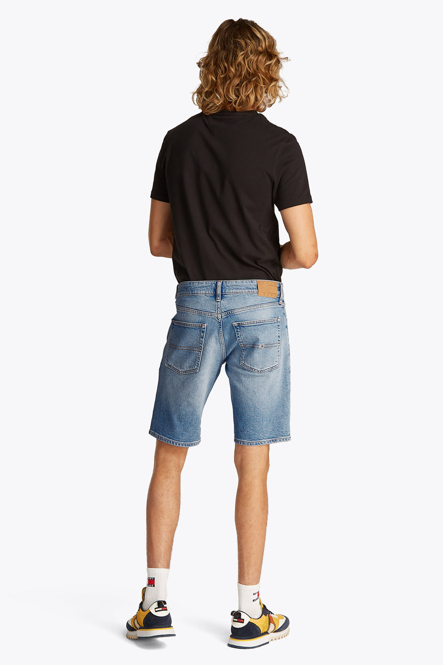 Jeansshort van lichtblauw denim van TOMMY JEANS, met achterzakken en gedragen met een zwart T-shirt en kleurrijke sneakers.
