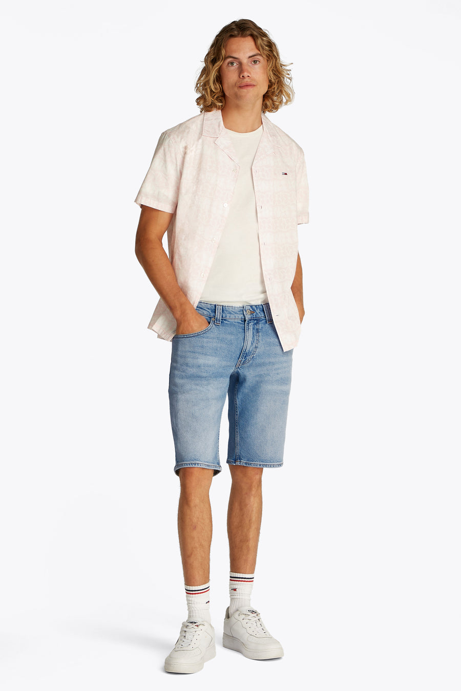 Jean court de denim bleu clair de TOMMY JEANS, avec des jambes courtes et porté avec un T-shirt blanc et une chemise rose.